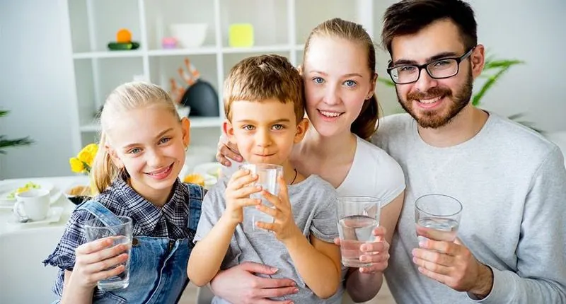A family smiling and holding glasses of clean water
